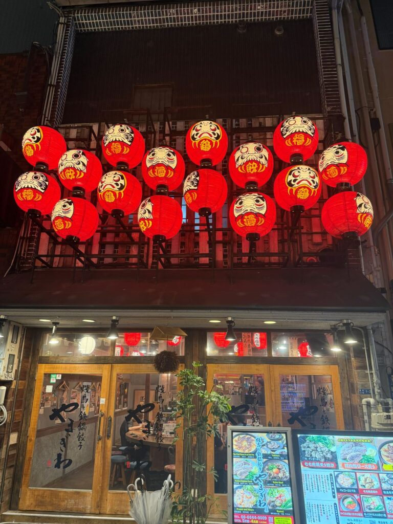 Lanterne rosse decorate con daruma sopra l ingresso di una izakaya di Osaka
