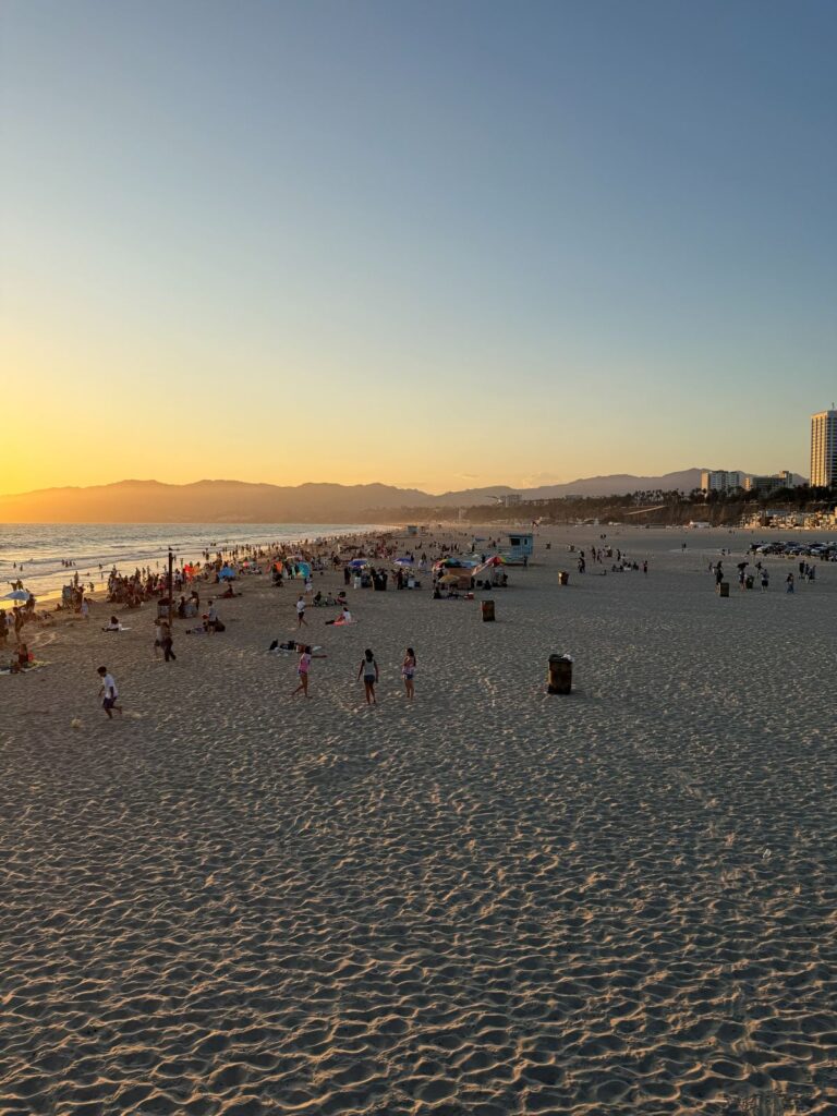 La spiaggia di Santa Monica affollata al tramonto con le montagne sullo sfondo